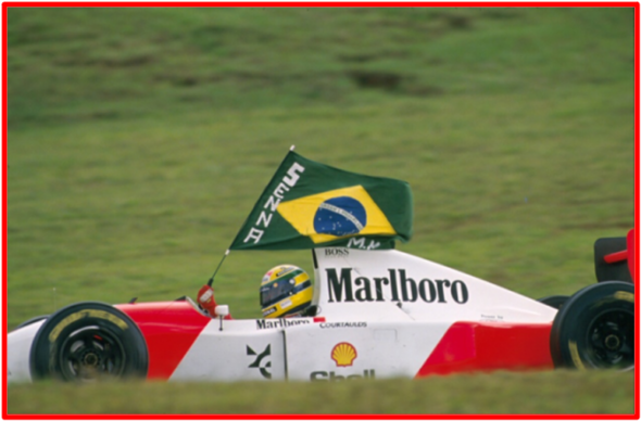 Ayrton Senna dans sa voiture de course agitant le drapeau brésilien : On pense que la feue légende était un patriote dans l’âme, un philanthrope, une personne véritablement de bon cœur. Au début de l’année 1994, Ayrton Senna a confié à sa sœur son projet de création d’une organisation caritative, qui investirait dans des programmes sociaux et dans l’éducation à travers le Brésil. Senna rêvait de voir chaque enfant et chaque jeune recevoir une éducation de qualité́. Photo Credit: 93BR_464 Fotógrafo Norio Koike 2008 -06DVD 